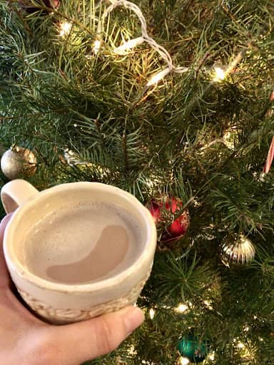 A mug of bone broth hot chocolate next to a lit Christmas tree
