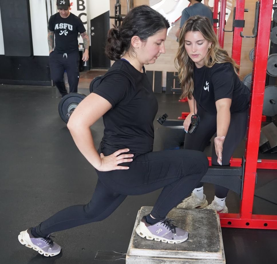 A personal trainer with a client doing a front foot elevated split squat, demonstrating the worth of personal training