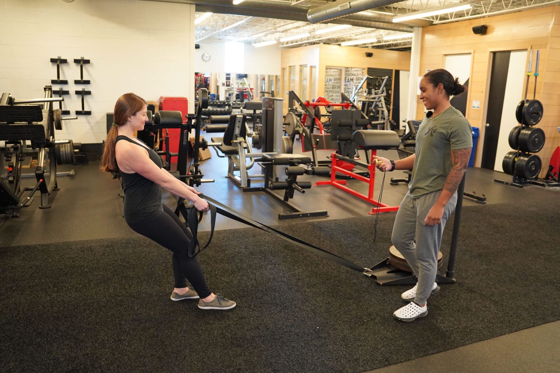 A client working on her knee joints dragging a sled as her trainer coaches her
